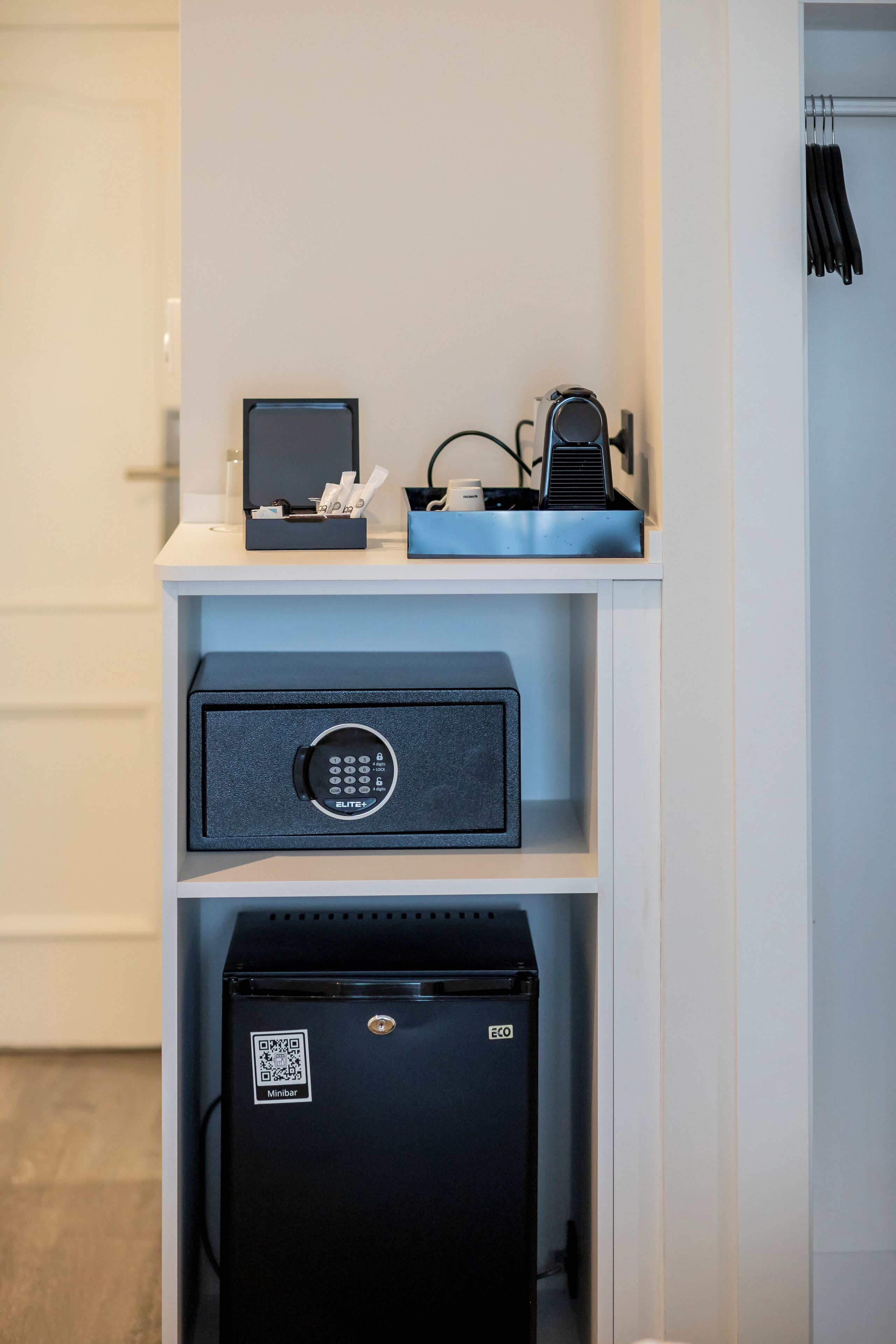 A minibar with a refrigerator, a safe, and a small table with a laptop and a phone.