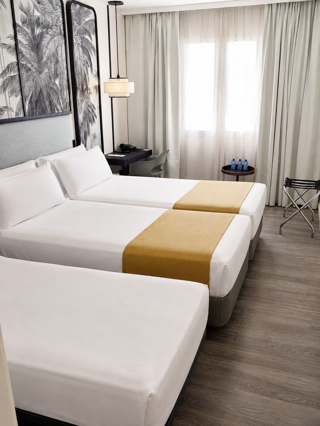 Ein Hotelzimmer mit zwei Betten, einem Schreibtisch, einem Stuhl, einer Lampe und einem Vorhangfenster.
