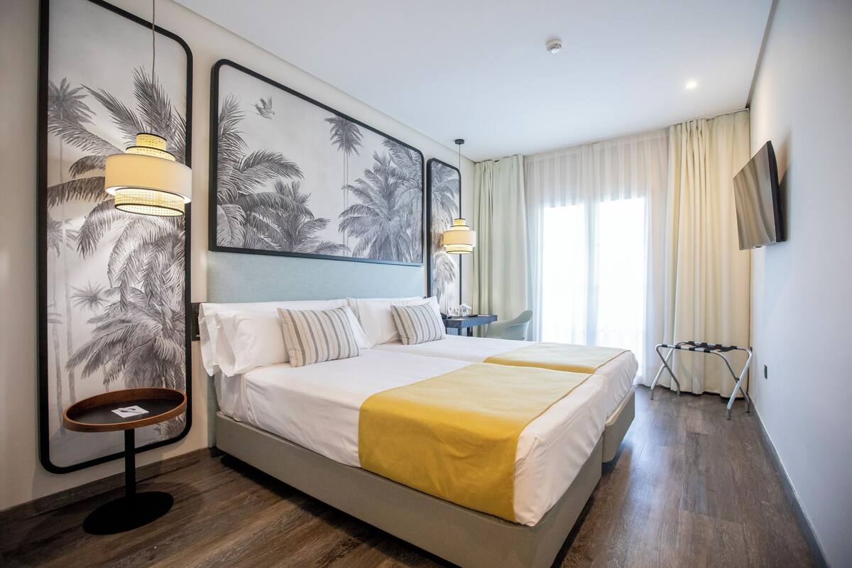 Habitación de hotel con una cama grande, dos mesitas de noche, un escritorio, una silla, un televisor y obras de arte en las paredes.