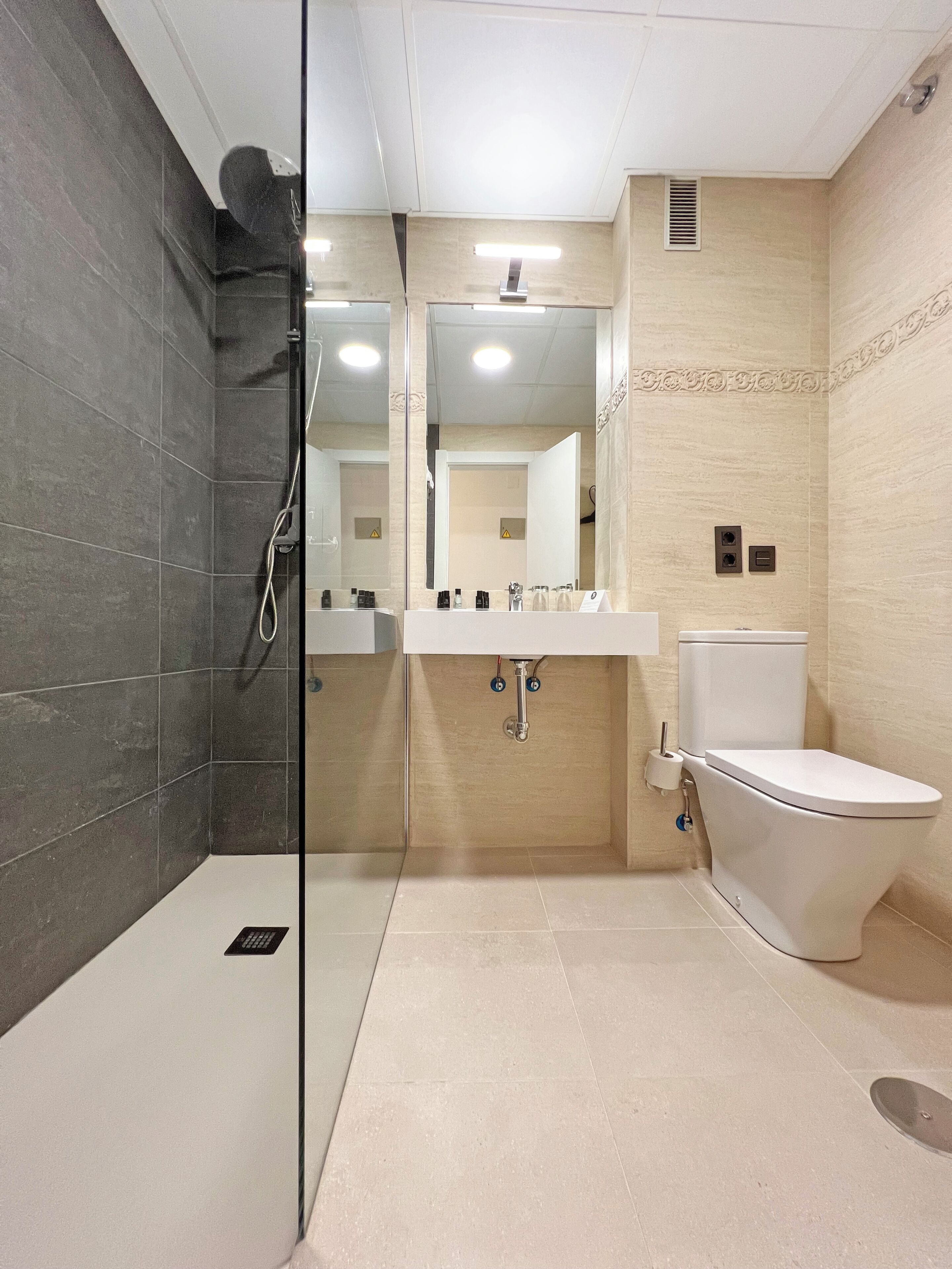 Une salle de bain moderne avec une douche à parois de verre, des toilettes blanches et un meuble-lavabo avec un miroir.