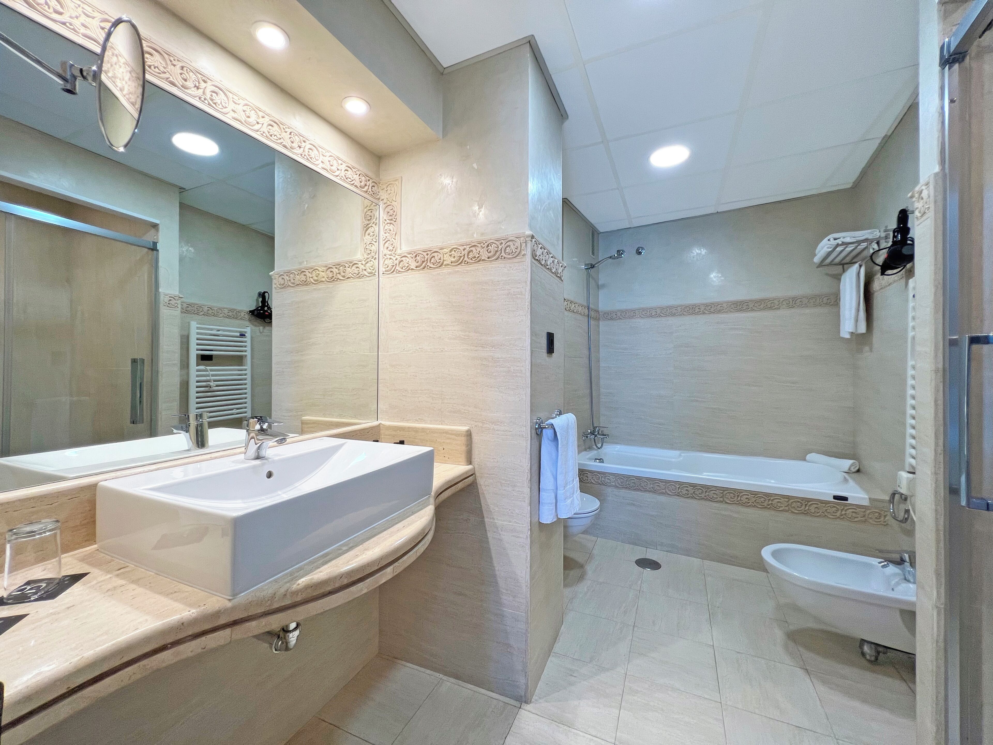 Ein modernes Badezimmer mit einem großzügigen Waschtisch, einer Badewanne, einer Dusche und einem separaten Handwaschbecken.