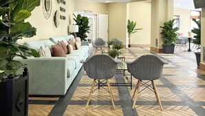 Een ruime lobby met een lichtgekleurde bank, gestreept fauteuils en potplanten.