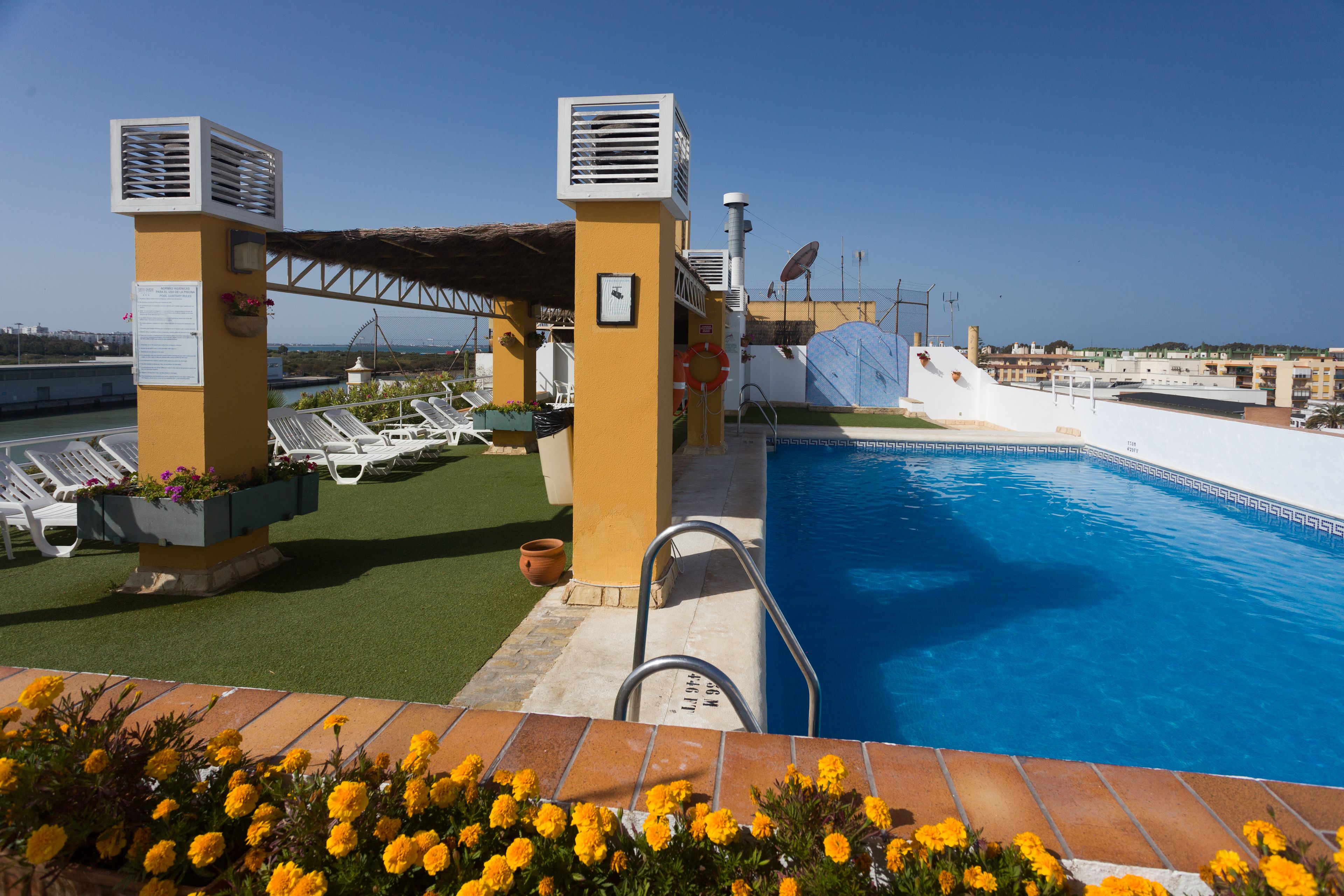 Un área de piscina en la azotea con sillones de descanso, piscina y vistas de la ciudad.