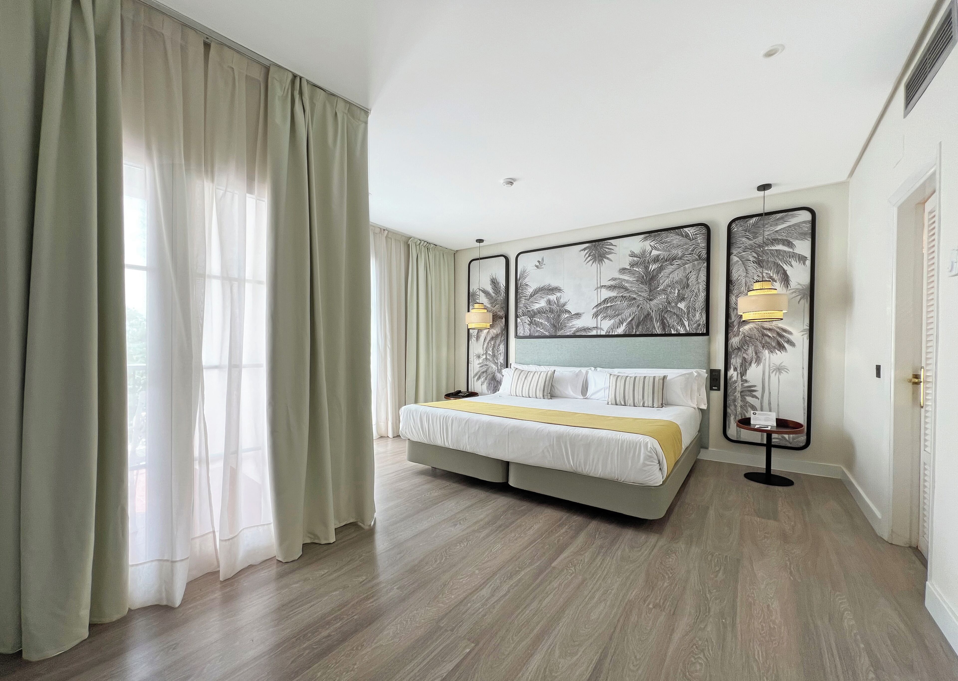 A hotel room with a large bed, two bedside lamps, and a large framed picture on the wall.