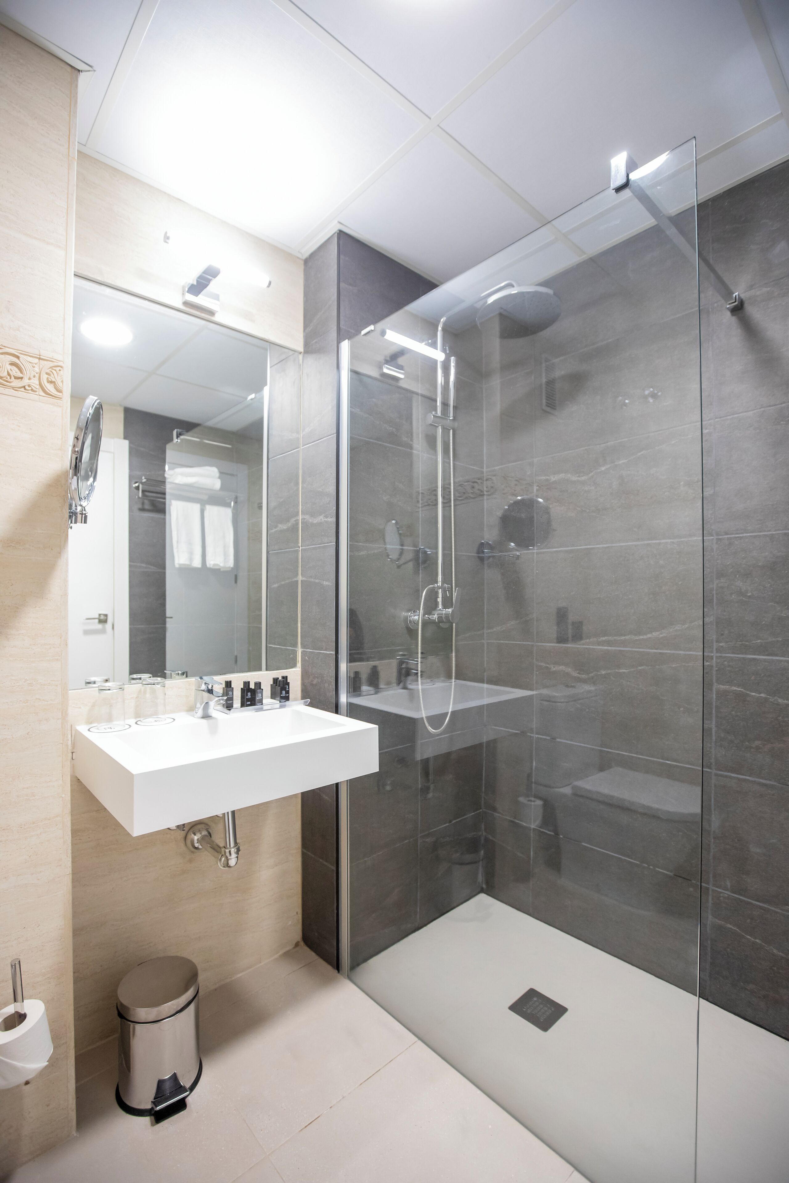 Un baño moderno con ducha de vidrio, un lavamanos blanco y un espejo encima.