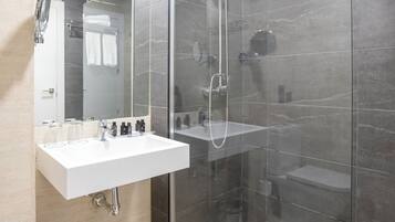Un baño moderno con ducha de vidrio, un lavamanos blanco y un espejo encima.