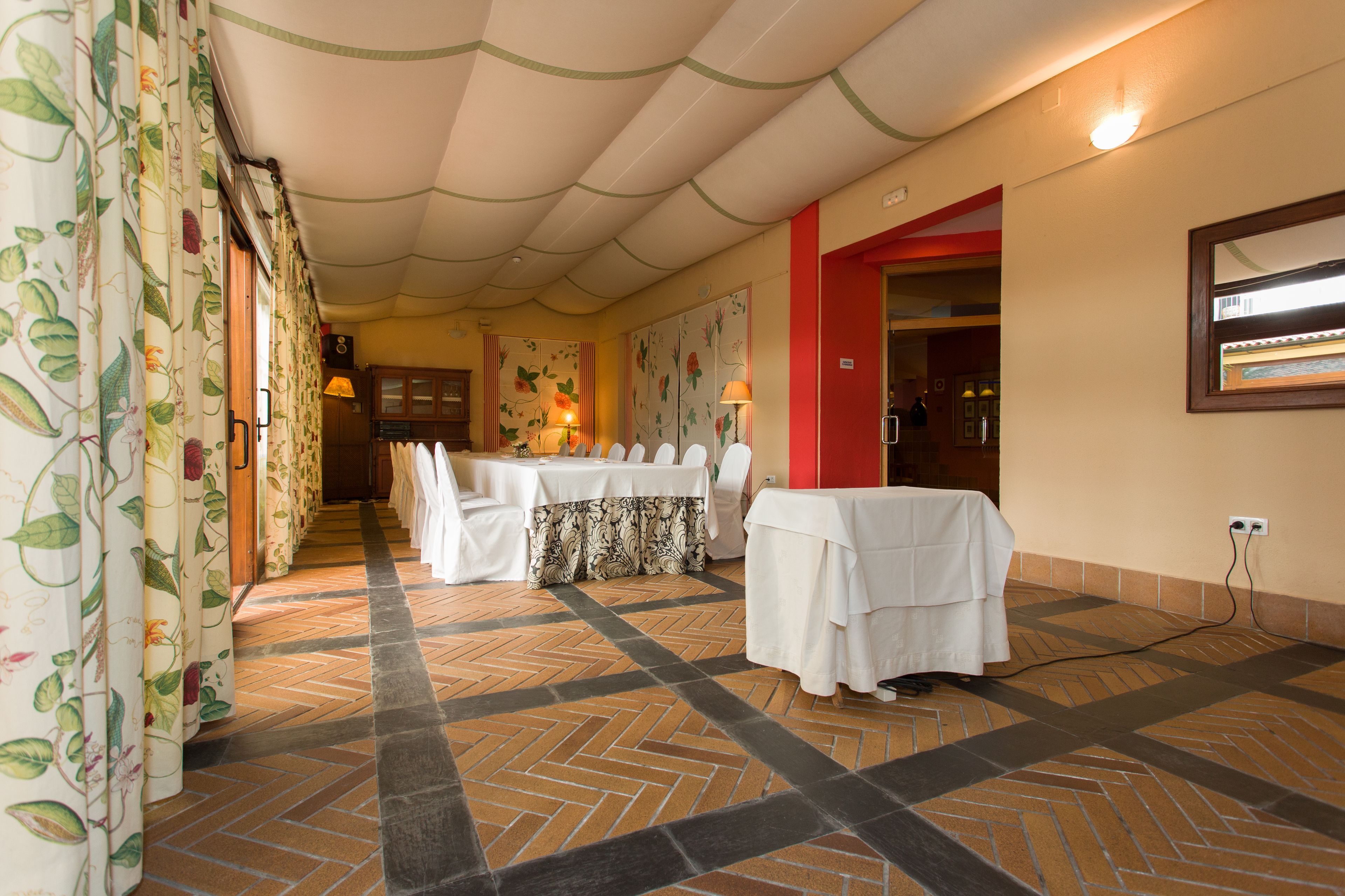 A hotel room with a tiled floor, a dining area with a table set for four, and a red accent wall.