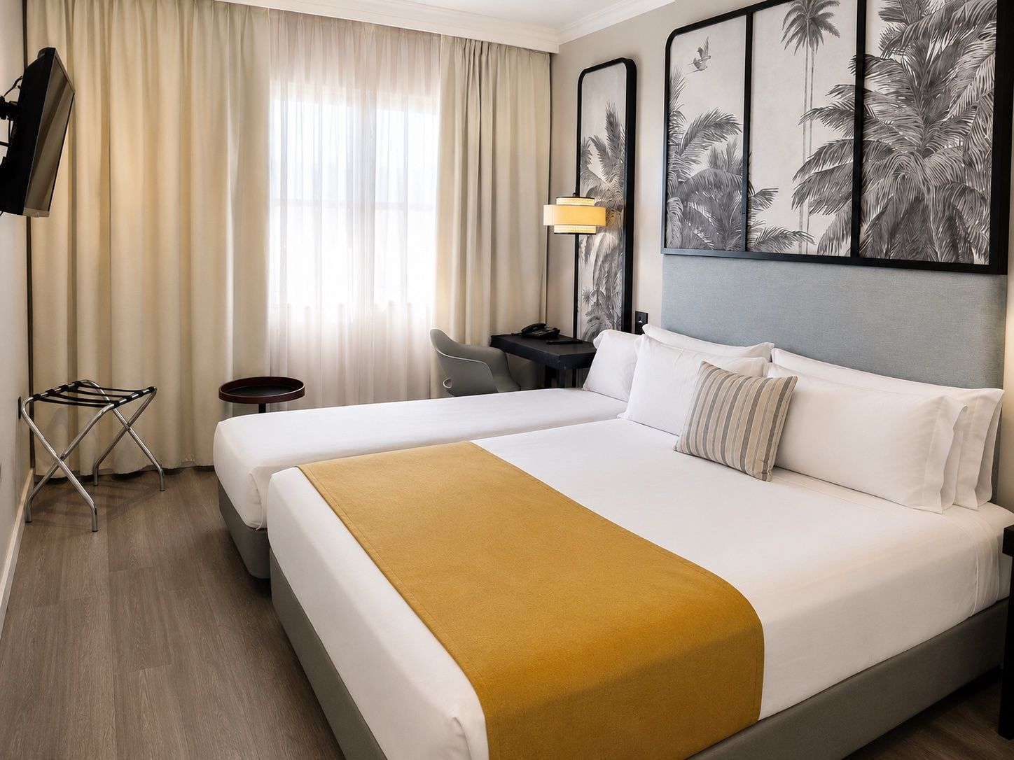 Habitación de hotel con dos camas, un escritorio, una silla, un televisor y un ventanal con cortinas.
