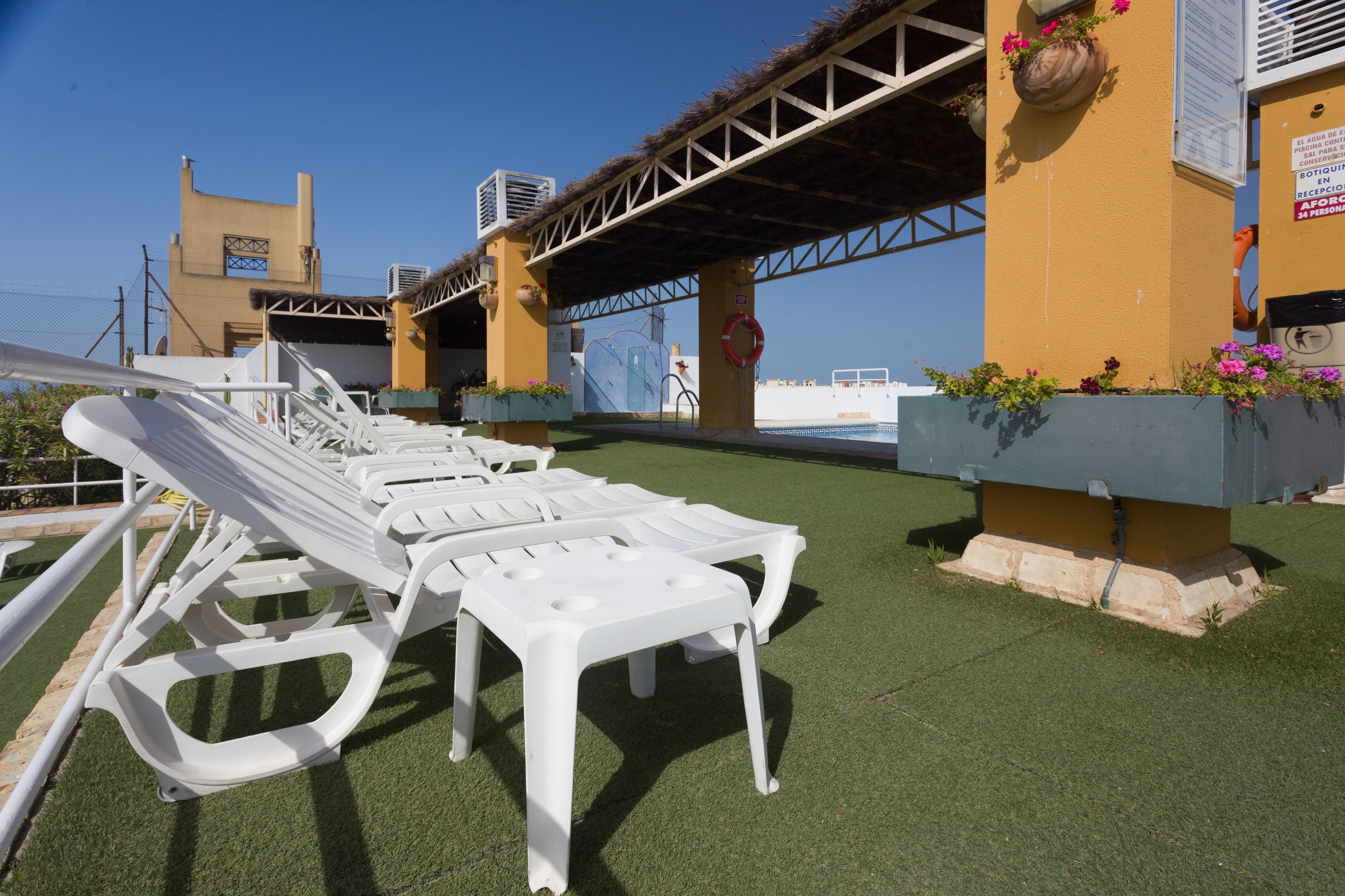 Un área junto a la piscina con sillones blancos y una zona de estar cubierta.