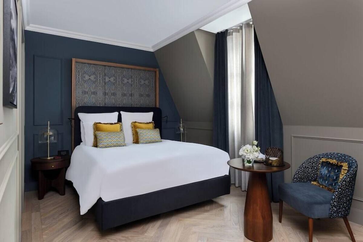 Un dormitorio con una cama grande, una mesa redonda de madera, una silla y un cabecero decorativo.