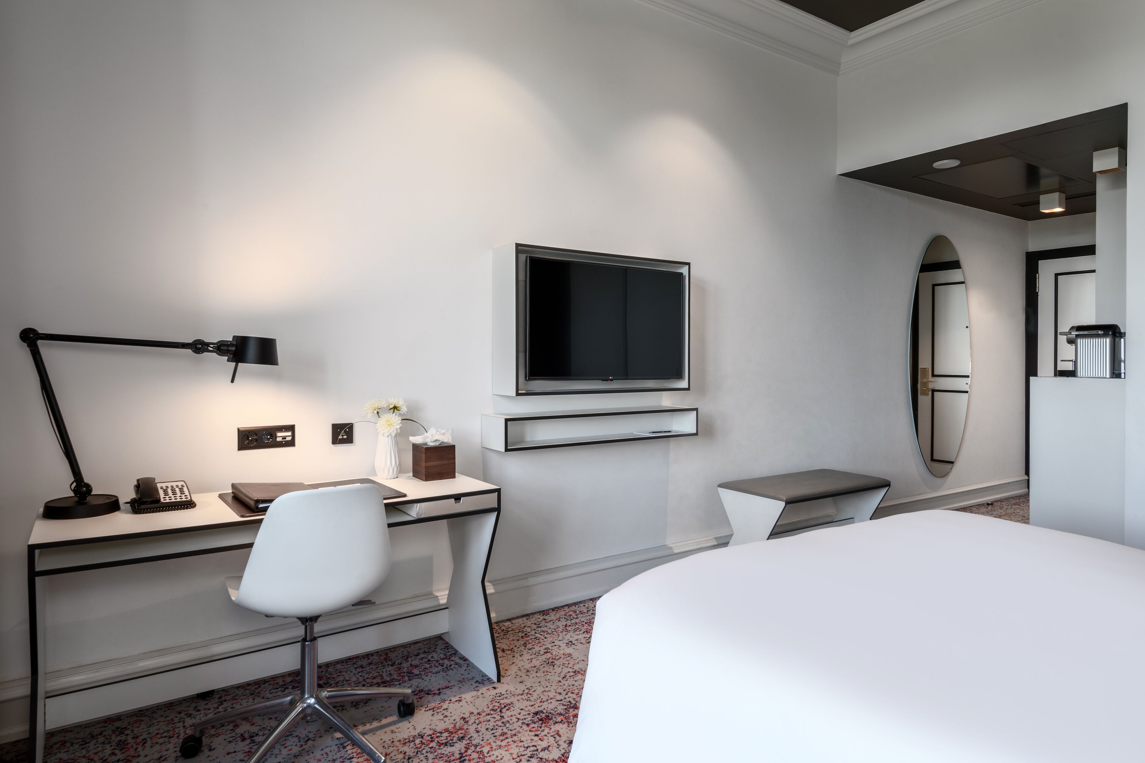 A modern hotel room with a desk, chair, TV, and bed.