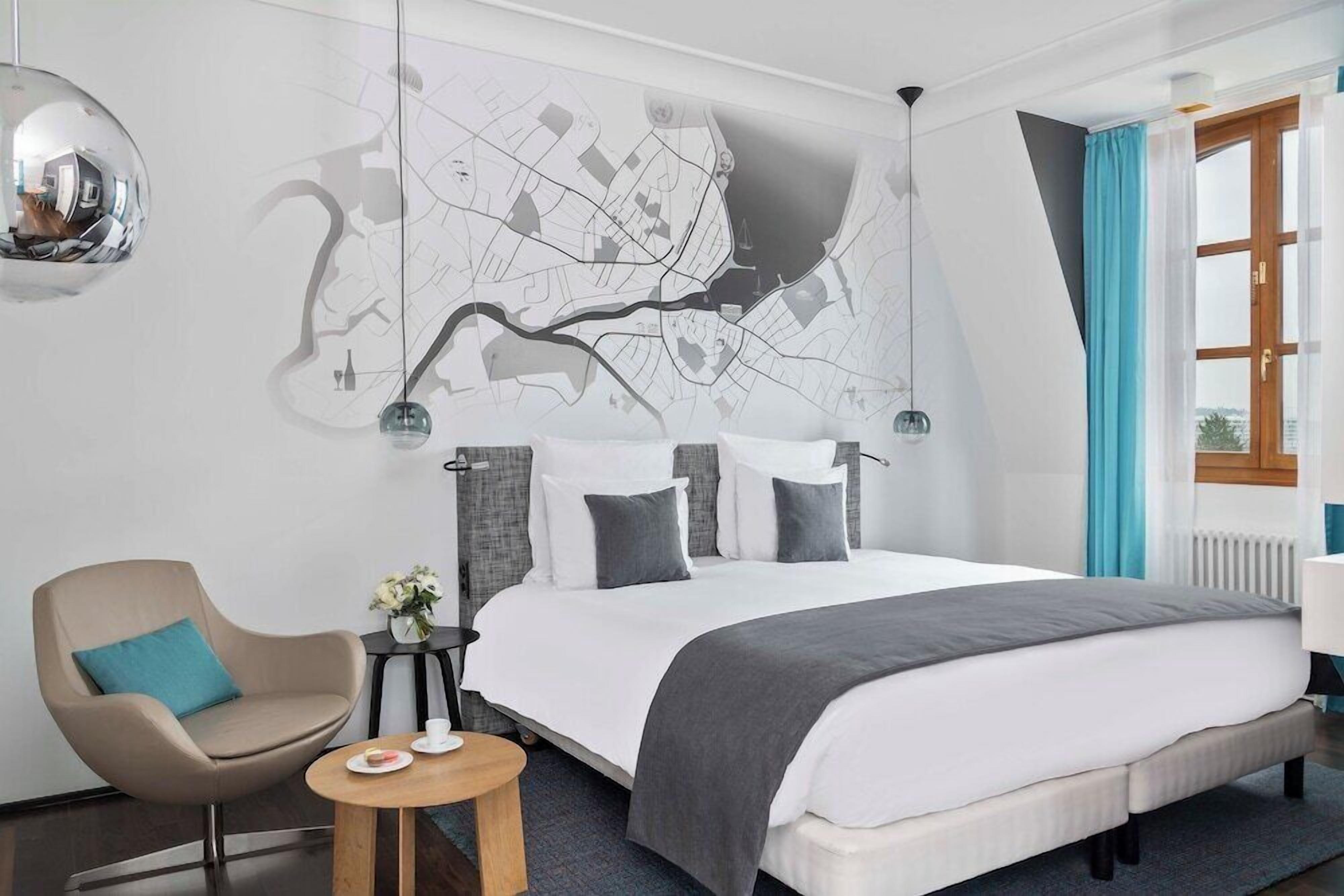 Een moderne hotelkamer met een groot bed, een zithoek met een fauteuil, een klein tafeltje en een kaart aan de muur.