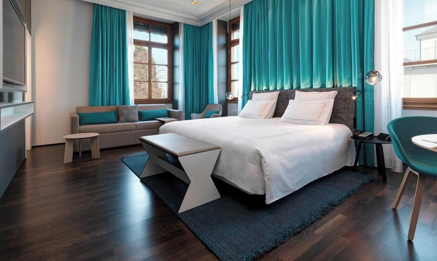 A modern hotel room with a large bed, a sofa, a small table, and a chair.