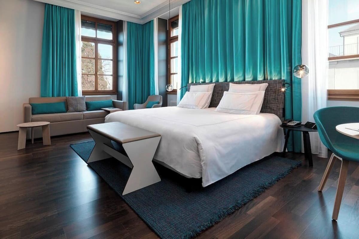 Ein modernes Hotelzimmer mit einem großen Bett, einer Sitzecke, einem kleinen Tisch und einem Sessel.