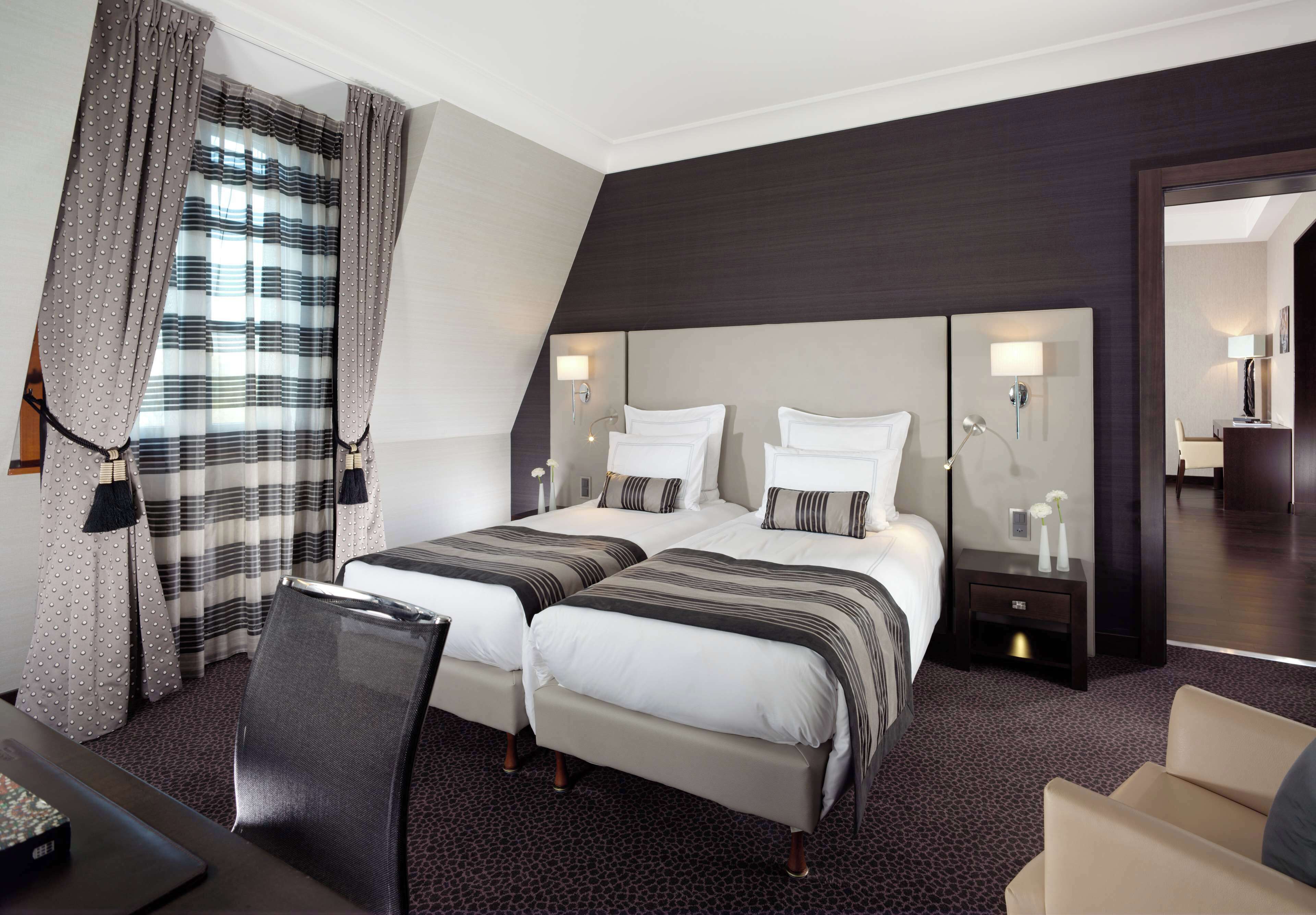 Ein Hotelzimmer mit zwei Betten, einem Schreibtisch, einem Stuhl, einem Spiegel und einem Nachttisch mit Lampe.