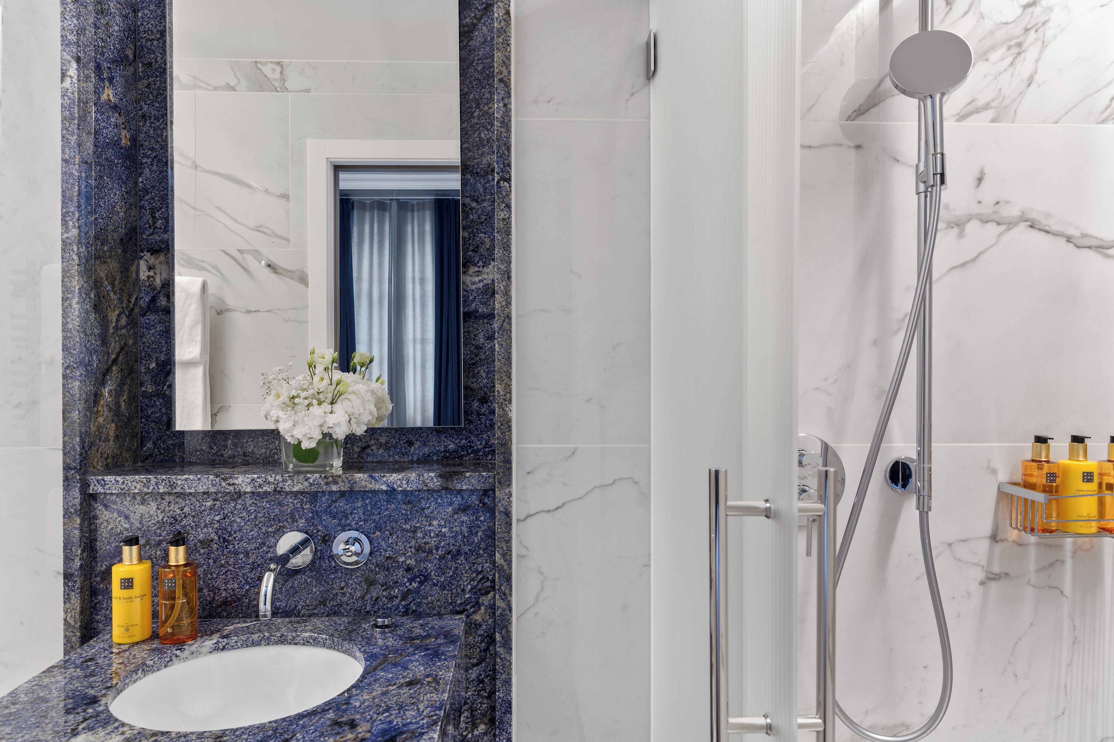 Un baño con lavamanos de mármol, un espejo, ducha y artículos de aseo en la pared.