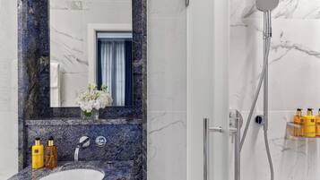 Un baño con lavamanos de mármol, un espejo, ducha y artículos de aseo en la pared.