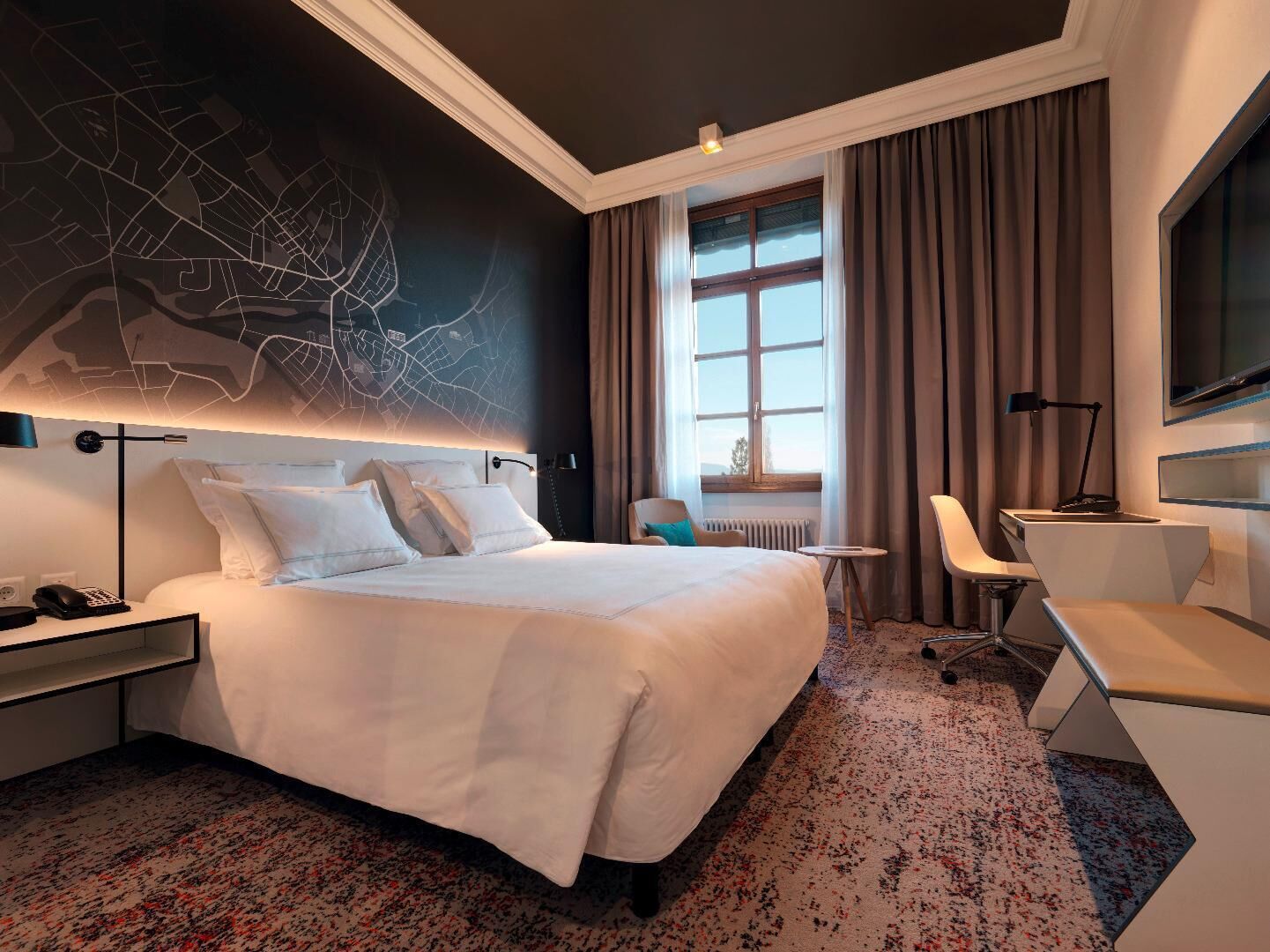 A hotel room with a large bed, a desk, a chair, a TV, and a map on the wall.