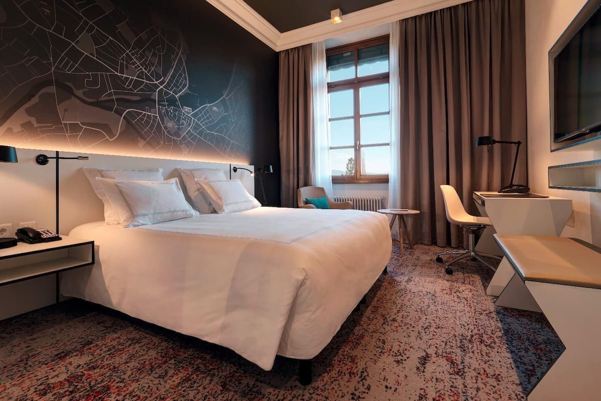 Ein Hotelzimmer mit einem großen Bett, einem Schreibtisch, einem Sessel, einem Fernseher und einer Karte an der Wand.