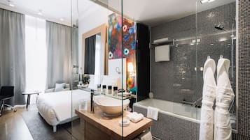 A modern hotel room with a large bed, a glass-enclosed shower, a wooden vanity, and a large mirror.