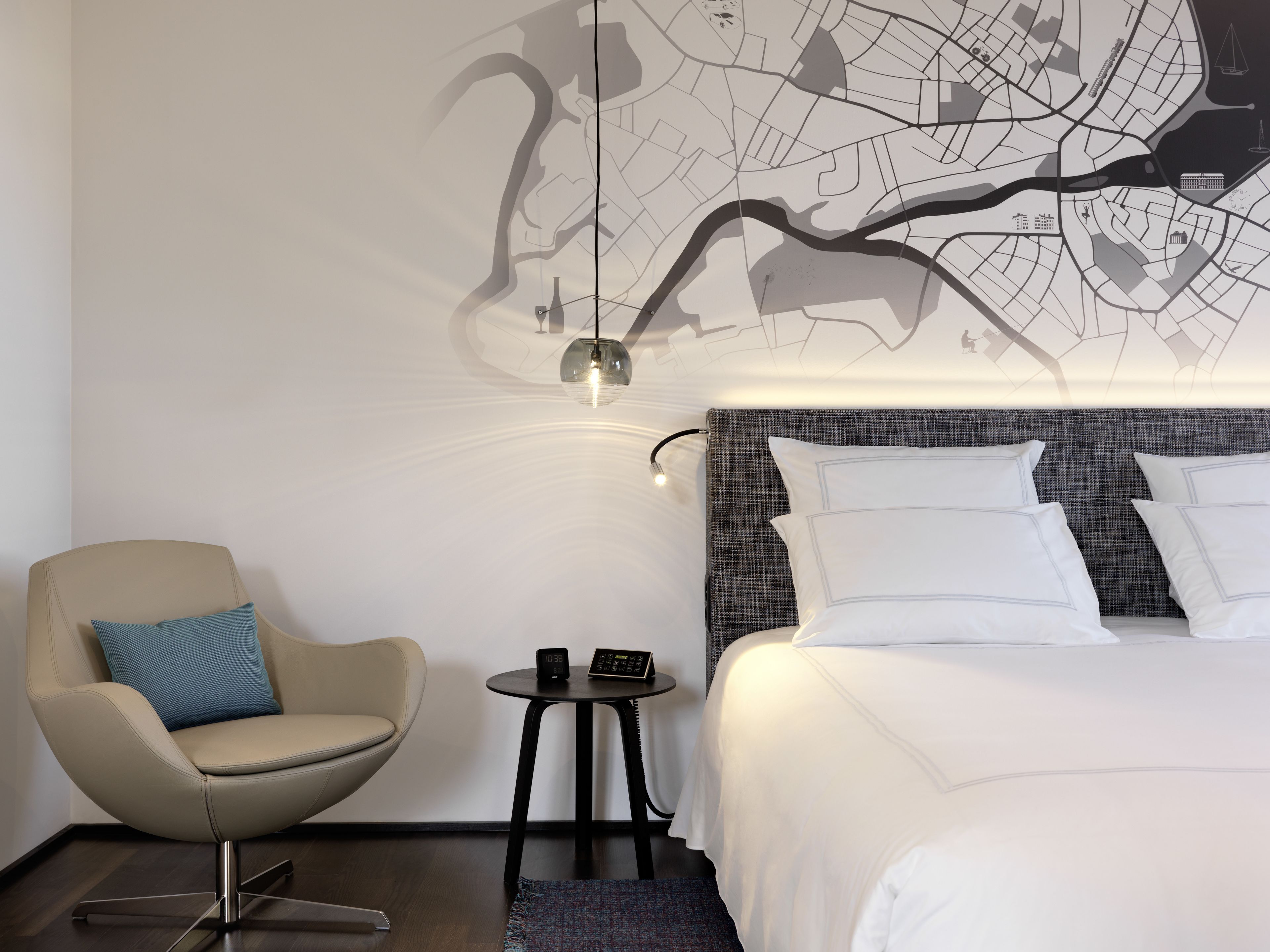 Ett modernt hotellrum med en stor säng, en stol, ett litet bord och en väggkarta.