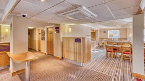 Un vestíbulo de hotel con una recepción, habitaciones privadas, un área de espera y un comedor.