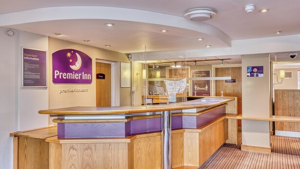 Un mostrador de recepción con acabado de madera, un letrero púrpura de Premier Inn y la puerta de una habitación privada.