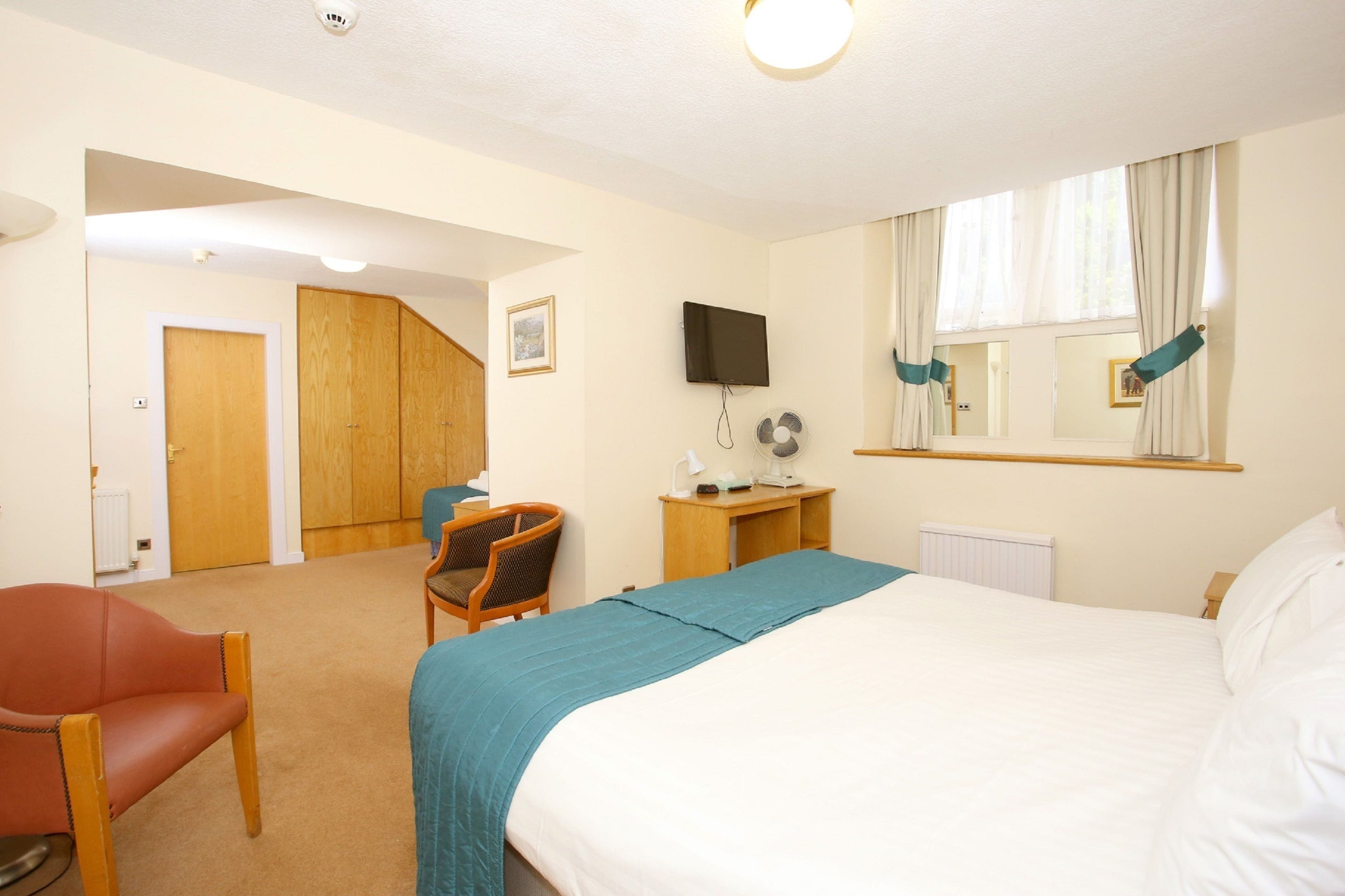 A hotel room with a bed, a desk, a chair, a television, and a window with curtains.