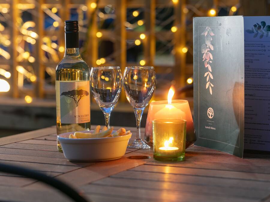 Una mesa con una botella de vino, dos copas, una vela y una carta.