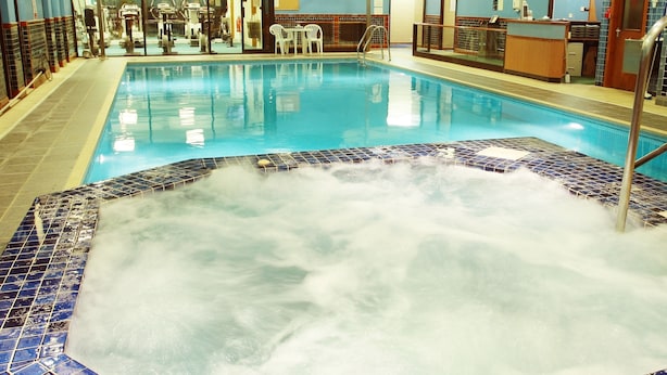 Une piscine intérieure dotée d’un espace avec jacuzzi, entourée de murs carrelés et comprenant un comptoir d’accueil.