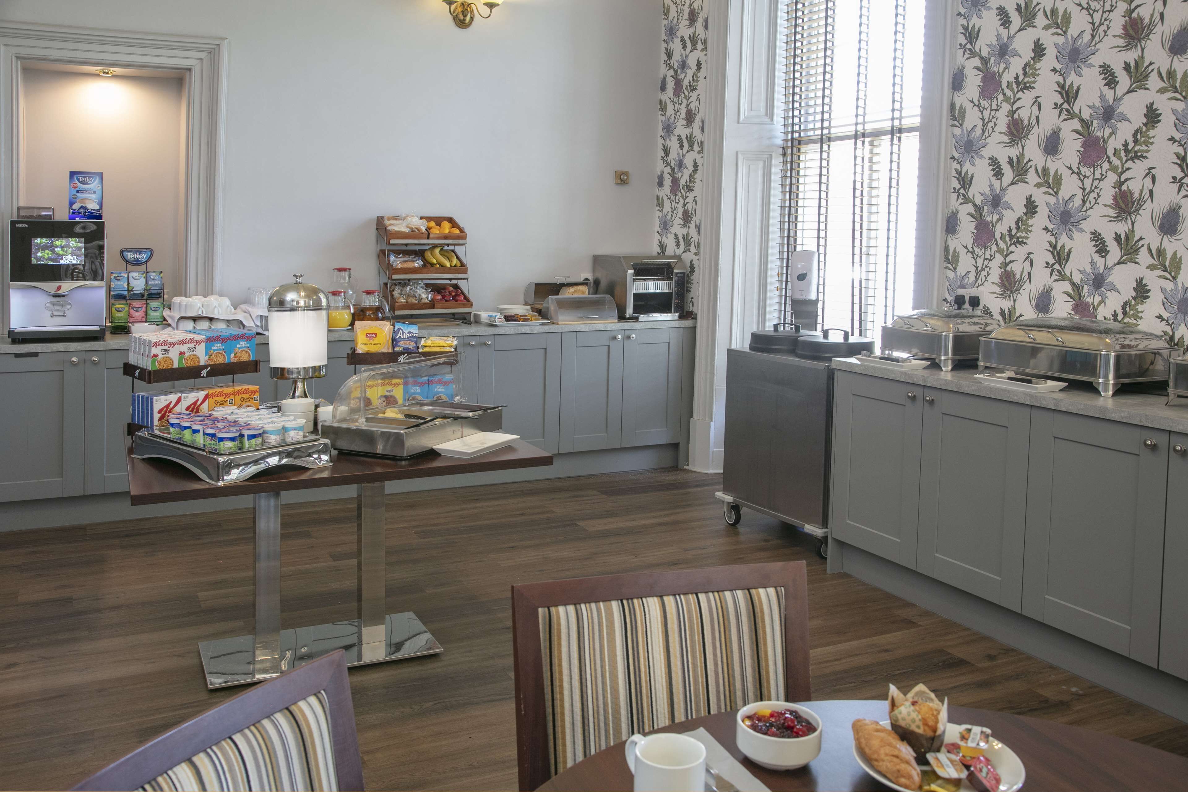 Espaço de café da manhã com serviço de buffet, incluindo cereais, frutas e doces.
