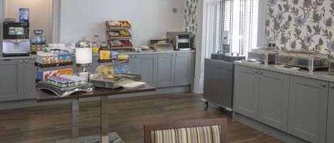 Espaço de café da manhã com serviço de buffet, incluindo cereais, frutas e doces.