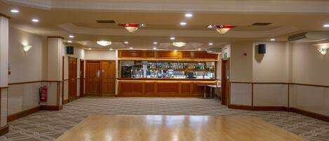 A spacious lobby with a large wooden reception desk, chandeliers, and patterned carpet.