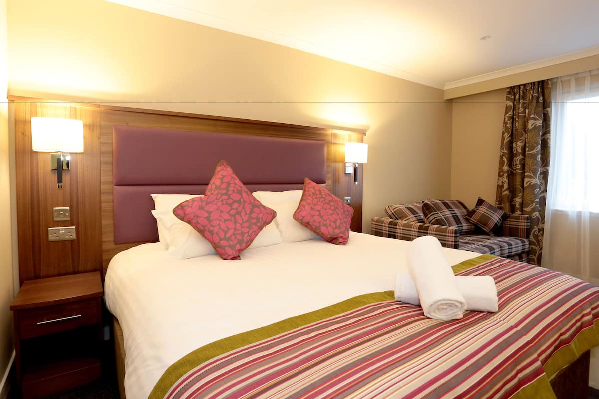 Habitació d'hotel amb un llit gran, una nitrera de fusta, una taula petita i una zona de seients amb un sofà i coixins.