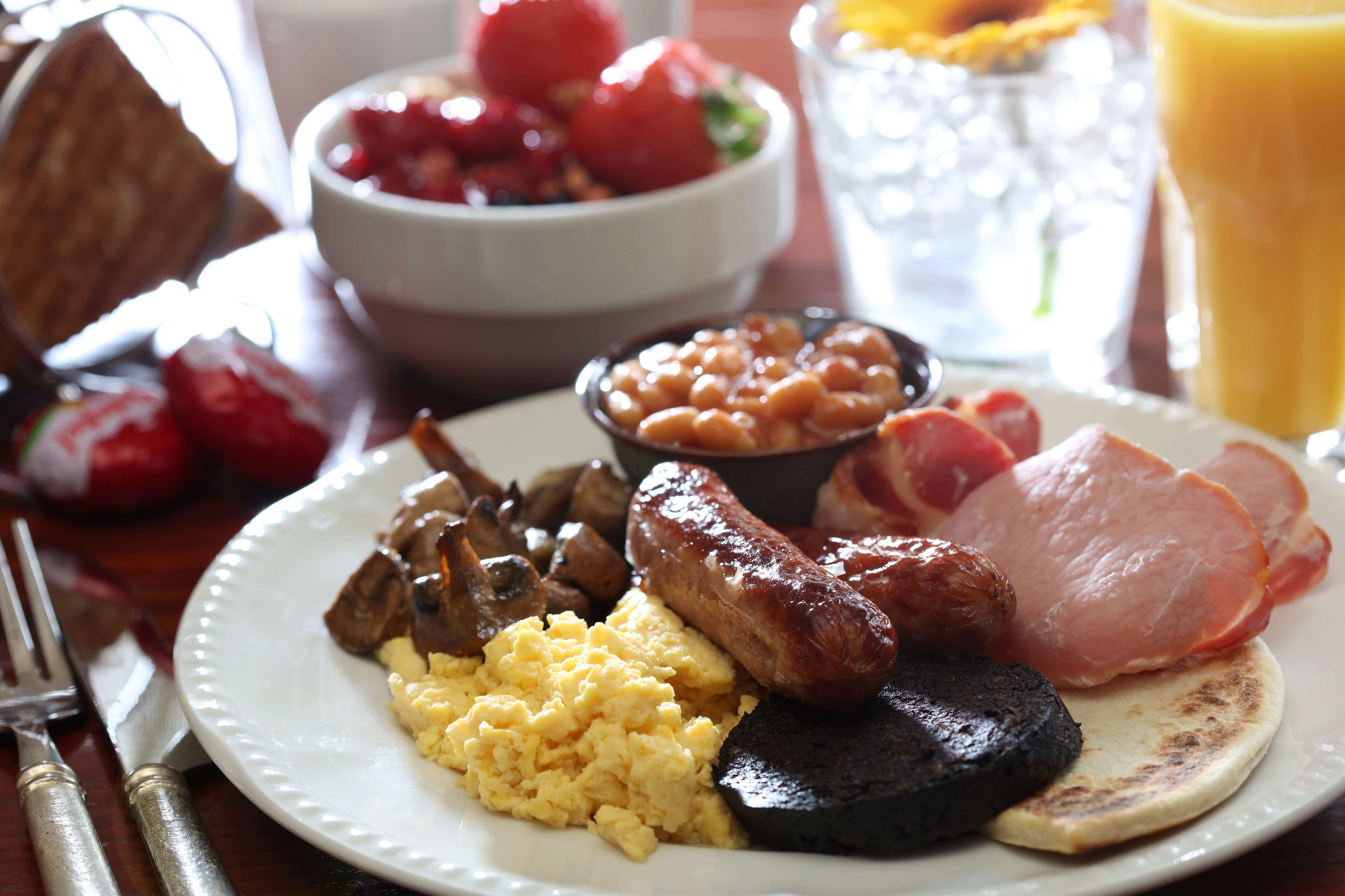 A plate with scrambled eggs, sausages, beans, and ham.