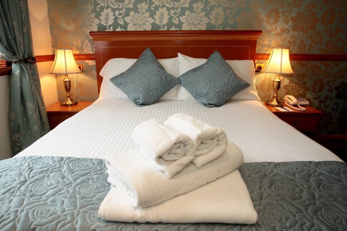 A neatly made bed with a folded towel, two pillows, and two bedside lamps.