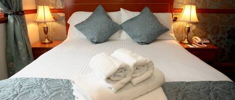 A neatly made bed with a folded towel, two pillows, and two bedside lamps.
