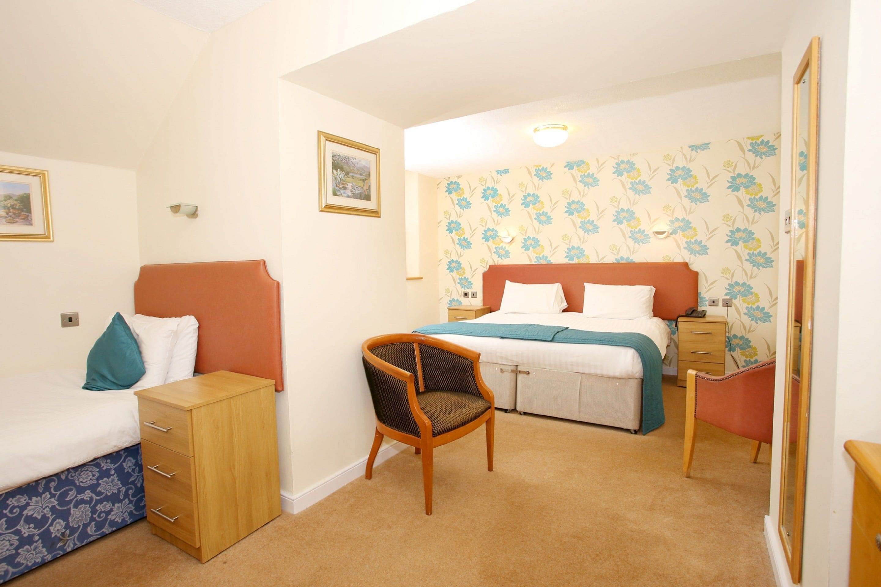 A bedroom with a bed, a wooden chest of drawers, a wicker chair, and a nightstand.