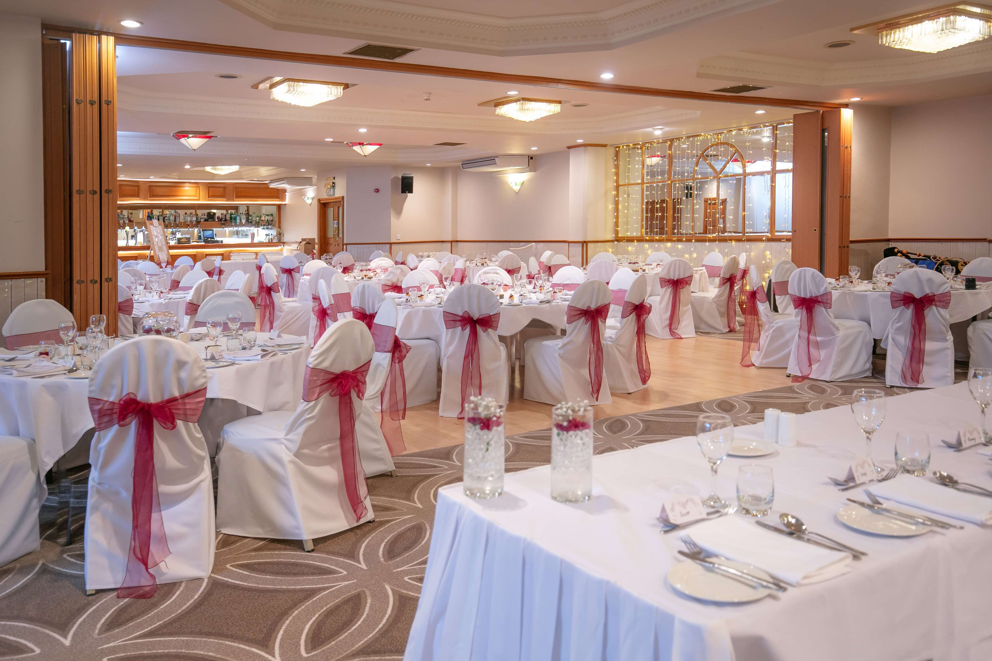 A banquet hall with round tables set for a formal event, featuring white tablecloths and chairs with pink sashes.