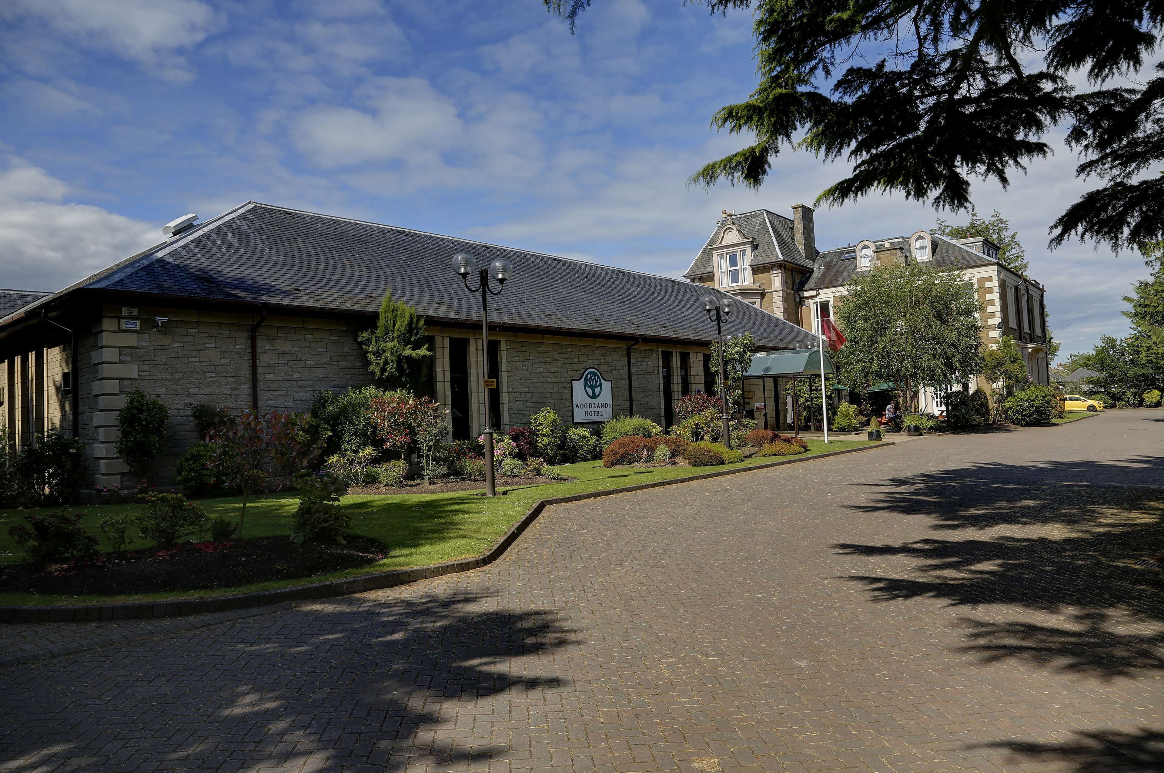 A hotel with a stone facade, a paved driveway, and a well-maintained garden.