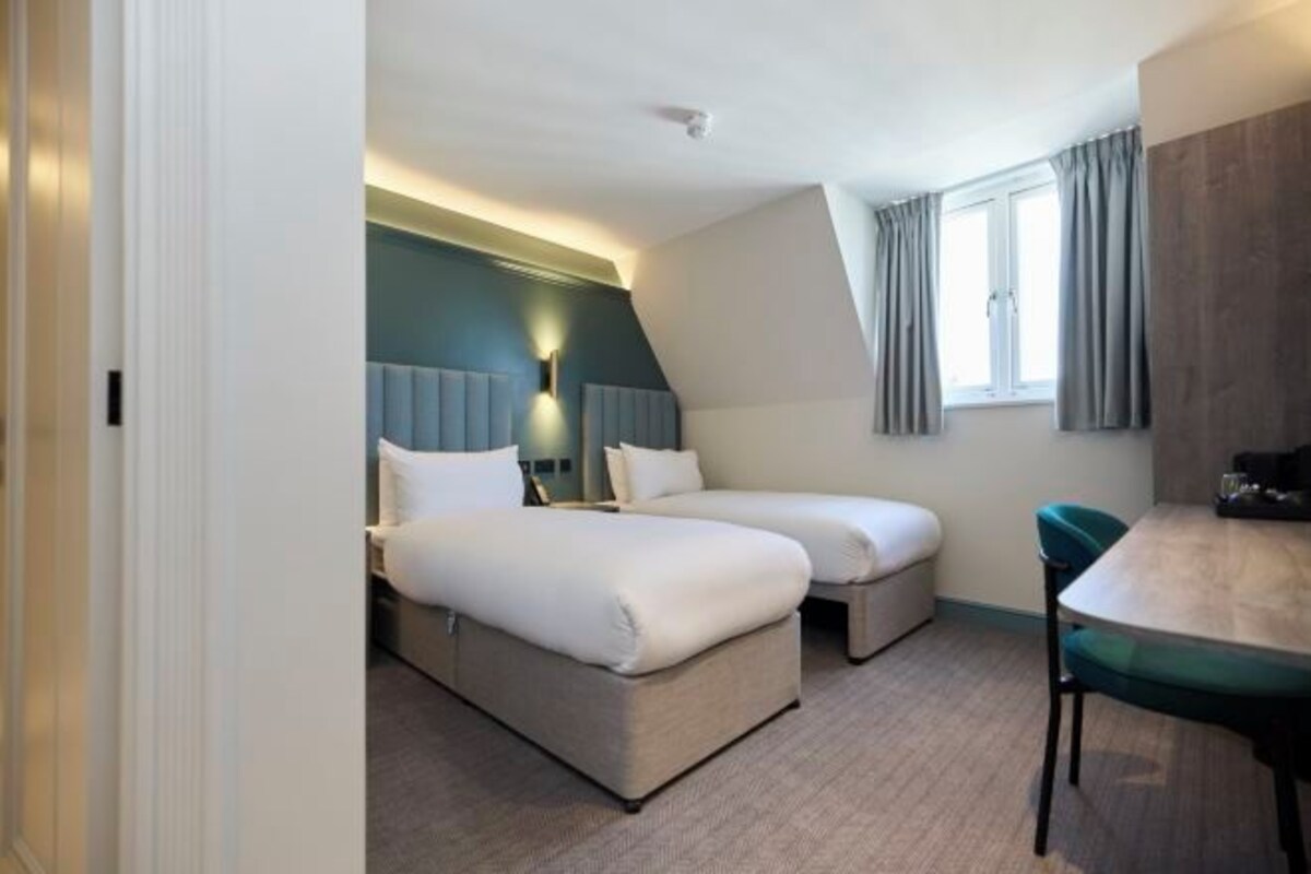 Ett hotellrum med två sängar, ett matbord och ett fönster med gardiner.