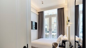 A hotel room with a bed, a desk with a computer and a coffee maker, a chair, and a large window with curtains. - The Edwin Hotel (London)
