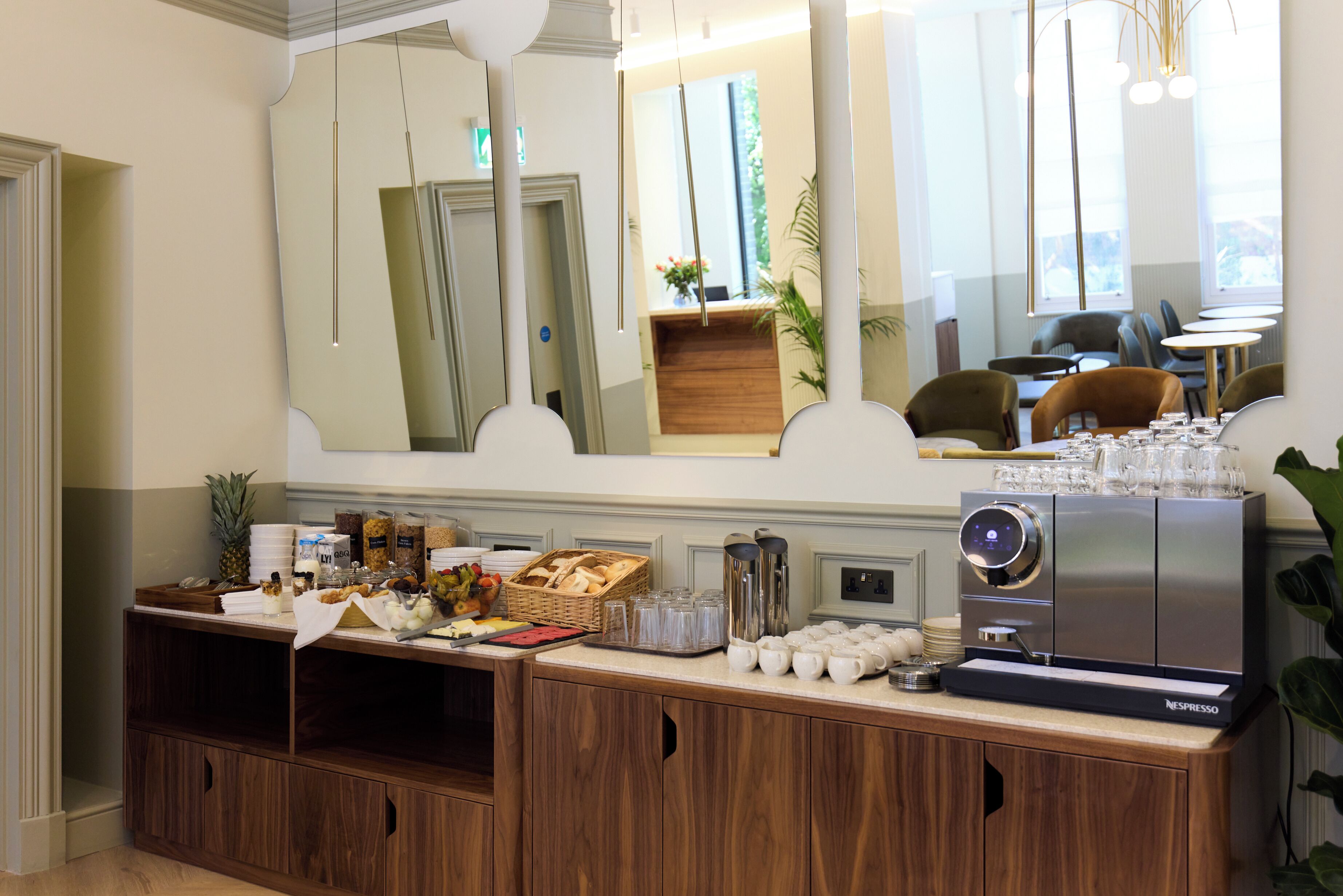 A breakfast buffet setup with a coffee machine, various food items, and a mirror reflecting the room.