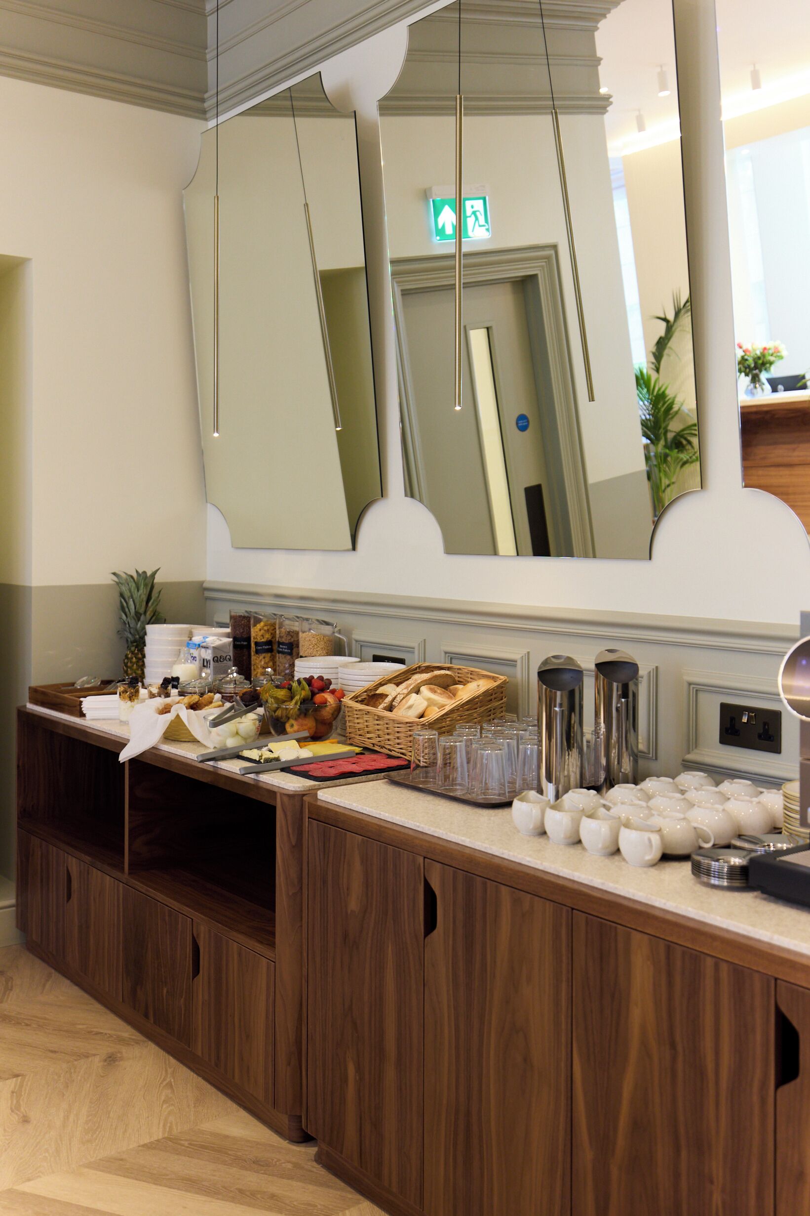 A breakfast buffet with various food items and beverages, a large mirror, and a wooden counter.