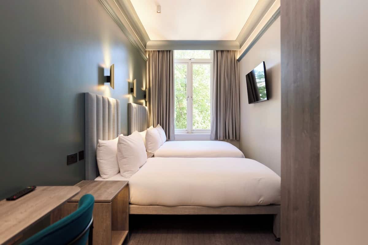A hotel room with a bed, a desk, a chair, a TV, and a window with curtains.