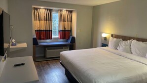 A hotel room with a bed, a desk, a chair, a window with curtains, and a nightstand with a lamp. - Microtel Inn by Wyndham Atlanta Airport (College Park)