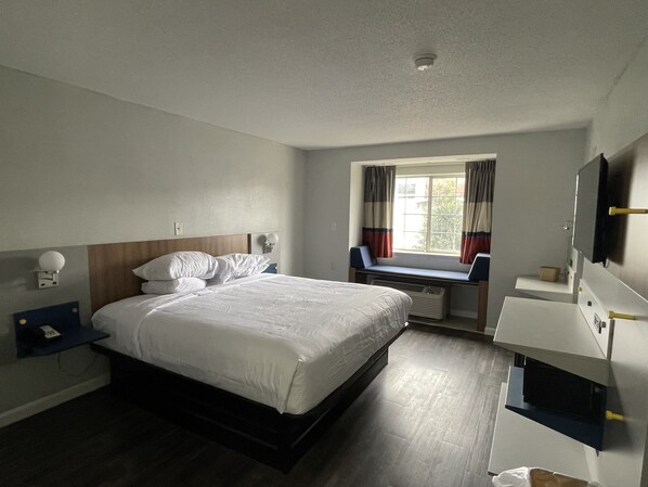 A hotel room with a bed, a desk, a window with curtains, and a mounted TV.
