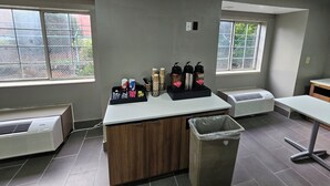 A kitchenette with a coffee station, a trash bin, and a window with a view of greenery. - Microtel Inn by Wyndham Atlanta Airport (College Park)