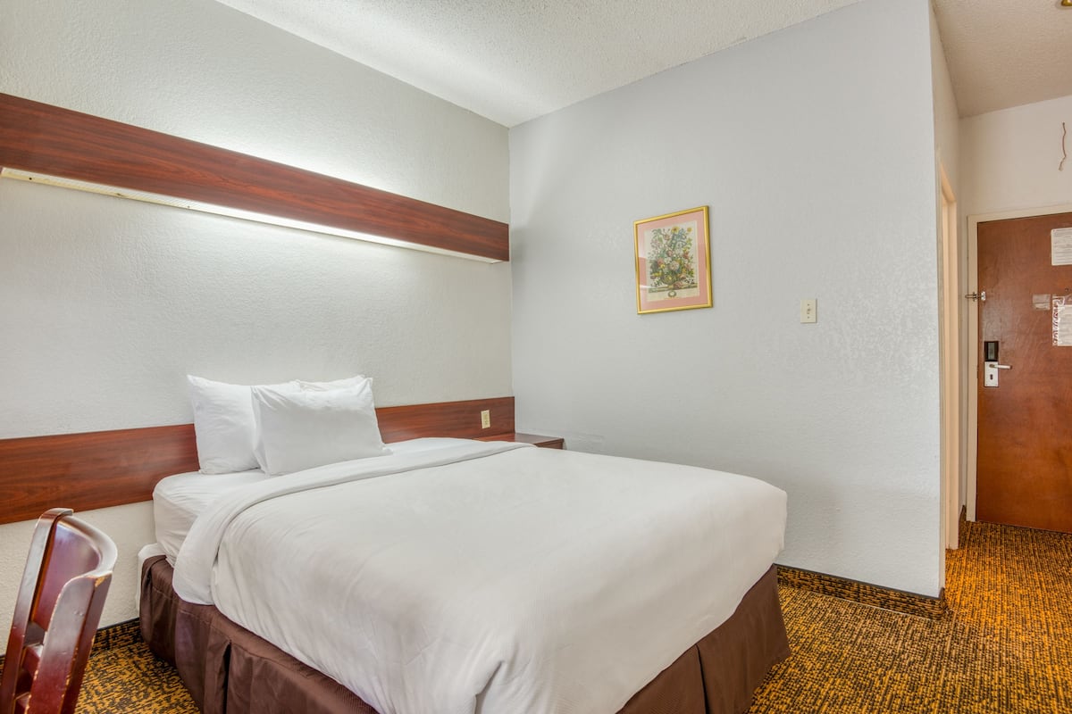 Quarto de hotel com uma cama de solteiro, cabeceira de madeira, quadro na parede e chão coberto de carpete.