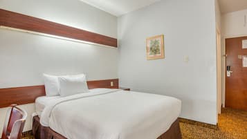 A hotel room with a single bed, a wooden headboard, a framed picture on the wall, and a carpeted floor.